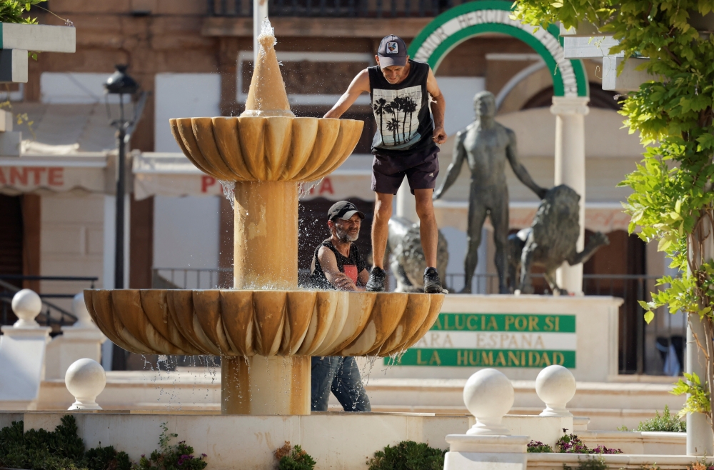 Men cool off in a fountain during the second heatwave of the year in Ronda, Spain. - Reuters