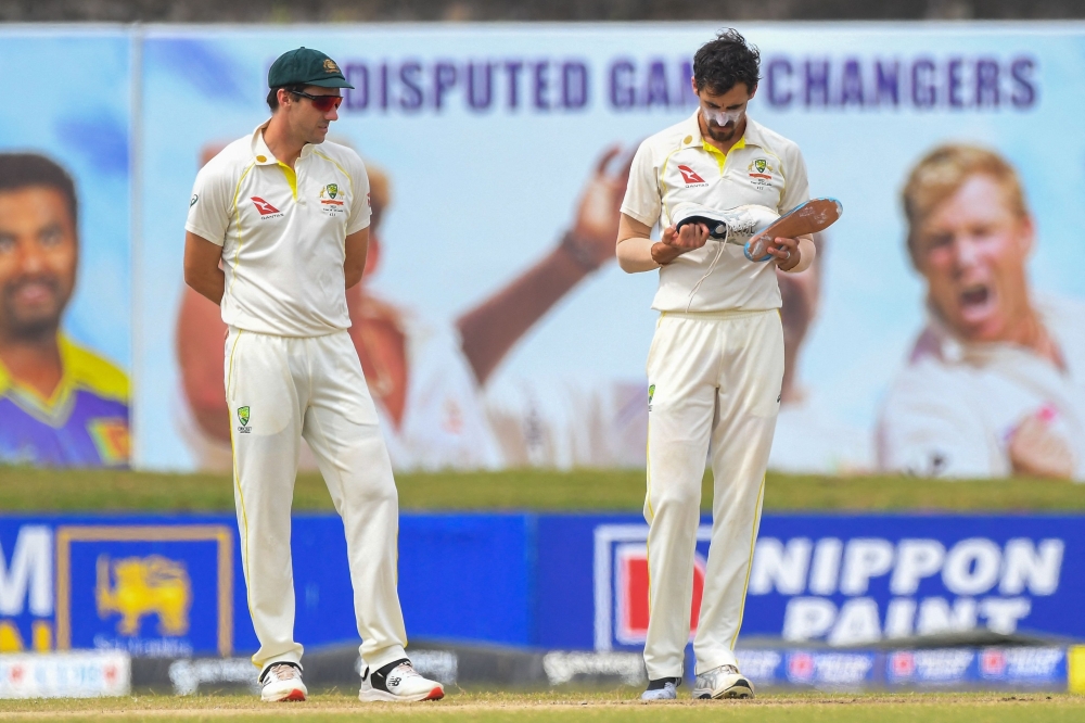 Australia's Mitchell Starc (R) holds his shoe as captain Pat Cummins watches during the fourth day of the second Test. -- AFP