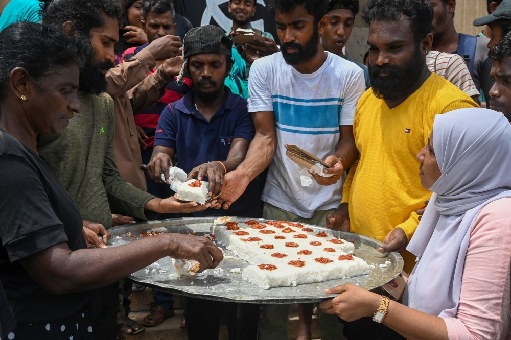 Demonstrators distribute auspicious milk rice as a part of the celebration after the resignation of ousted Sri Lanka's President Gotabaya Rajapaksa at the Presidential Secretariat in Colombo on July 15, 2022.