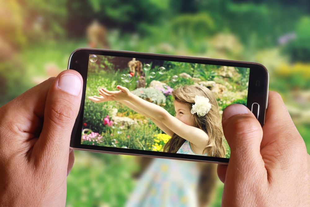 Male hand taking photo of Vintage Portrait of beautiful girl blowing bubbles with cell, mobile phone. Kids, childhood, family concept.
