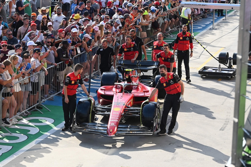 Fans look on as the car of Ferrari's Spanish driver Carlos Sainz Jr is pushed by team members during the Pit Lane Walk ahead of the Formula One Hungarian Grand Prix at the Hungaroring in Budapest on July 28, 2022.  (Photo by ATTILA KISBENEDEK / AFP)