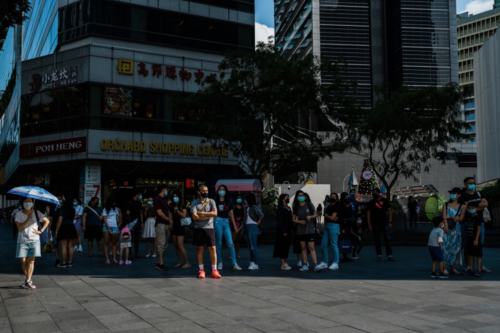People wait in the shade before crossing the street in Singapore, Dec. 16, 2021. (Gabriela Bhaskar/The New York Times)