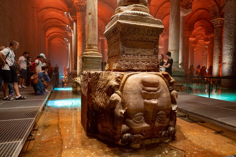 People stands next to the Medusa head in the Basilica Cistern while visiting the historic site in Istanbul, Turkey, on July 26, 2022. Built in 542 and resting near the Hagia Sophia -- then a cathedral, now a mosques -- the basilica was once part of a network of more than 100 cisterns begun by the Romans and completed by the Byzantians and Ottomans to supply the city and its palaces with running water. (Photo by Yasin AKGUL / AFP)