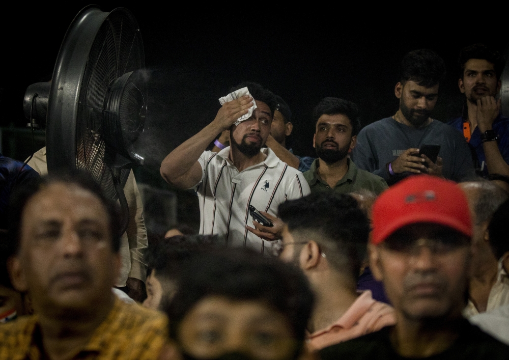 A spectator stands next to a mist fan and wipes sweat off his face during a game between India and South Africa at Arun Jaitley Stadium in New Delhi, on June 9, 2022. (Anindito Mukherjee/The New York Times)