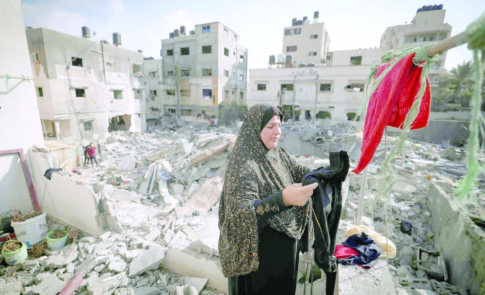 A Palestinian woman looks for salvageable items amid the rubble outside her home, heavily damaged in Israeli air strikes. -- AFP 