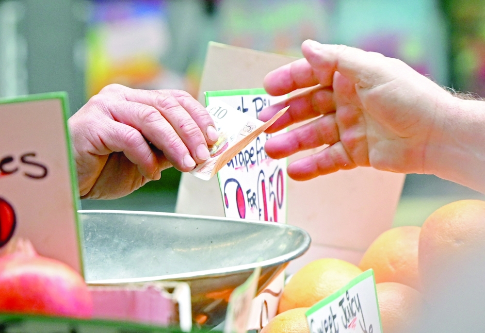 A customer pays for his fruit and vegetables with a ten pound sterling note, at a trader's market stall in London. - AFP