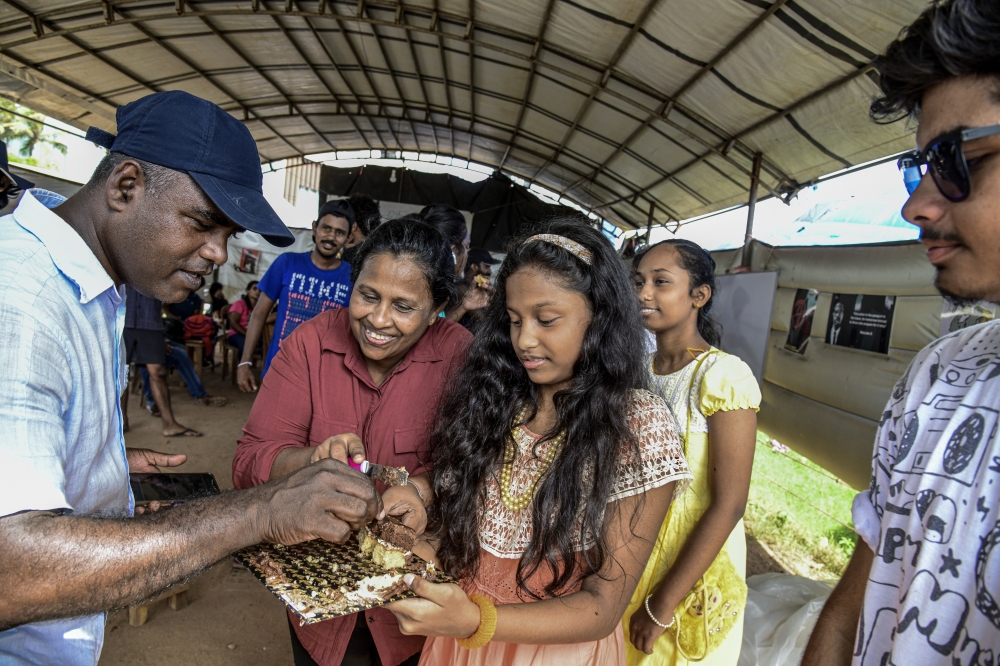 Dhammika Muthukumarana, second from left, and her daughters, Sanuli, center, and Dulini, right, offer a birthday cake to the people at the Galle Face protest site in Colombo, Sri Lanka, on July 16, 2022. (Atul Loke/The New York Times)