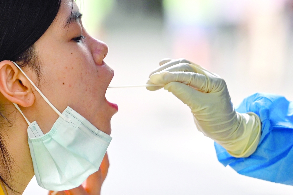 A health worker takes a swab sample from a woman to test for the Covid-19 coronavirus in the Huangpu district of Shanghai on August 17, 2022. (Photo by Hector RETAMAL / AFP)