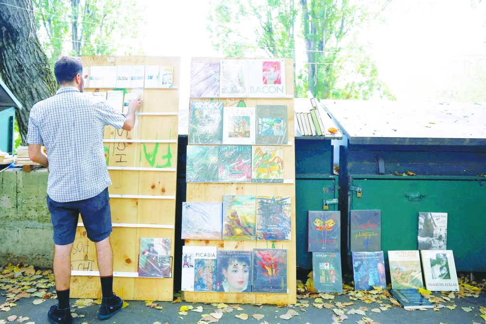 New Parisian bouquiniste, traditional street bookseller, places books on shelves along the banks of the River Seine in Paris