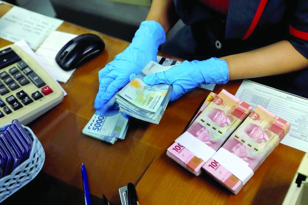 An employee wearing a face mask and synthetic gloves counts Indonesia's rupiah banknotes at a currency exchange office in Jakarta. — Reuters