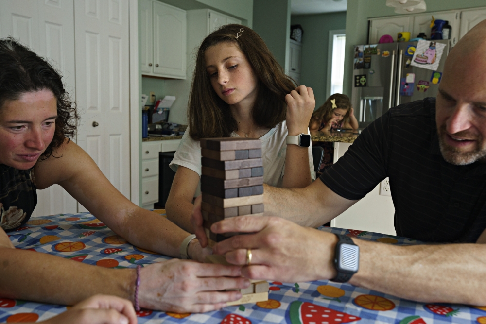 Catie Desi, center, plays a game of Jenga at the kitchen table with her parents and younger brother in Cokeysville, Md. on Aug. 26, 2022. (Melissa Lyttle/The New York Times)