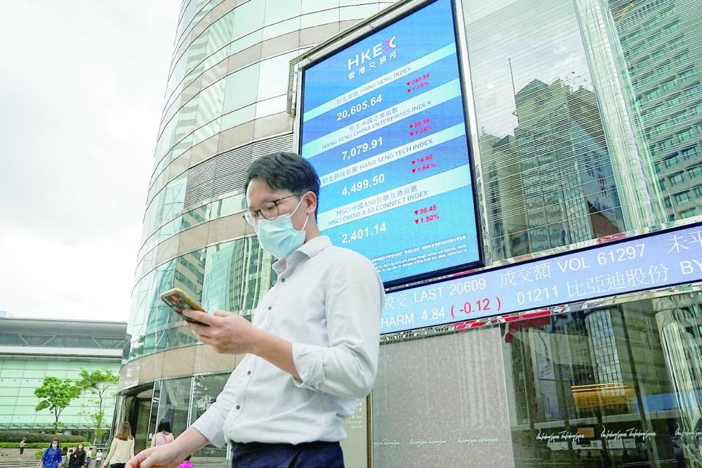 People walk past a screen displaying the Hang Seng stock index outside Hong Kong Exchanges. - Reuters