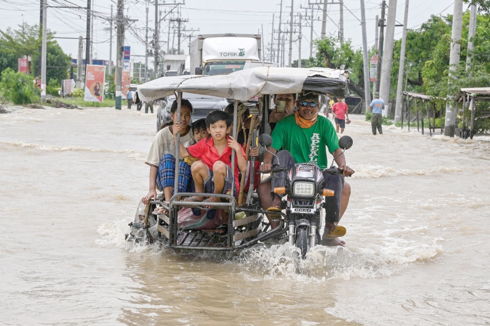Residents and motorists commute along a flooded highway in the aftermath of Super Typhoon Noru in San Ildefonso, Bulacan province. — AFP

