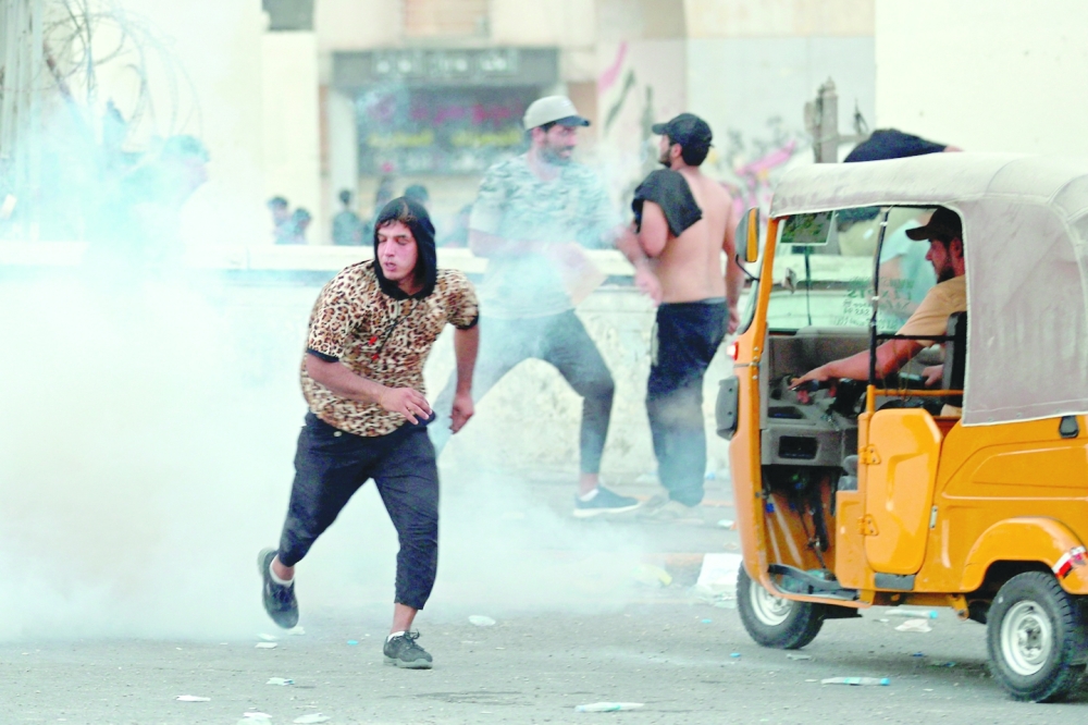 Supporters of Moqtada run for cover from tear gas fired by Iraqi security forces amid clashes in Tahrir Square in Baghdad during a parliament session. - AFP