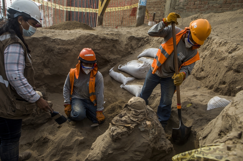 Carlos Lalangui, right, digs around the remains of a funerary bundle in an ancient tomb discovered beneath a street in a residential district north of Lima, Peru, Sept. 30, 2022. (Marco Garro/The New York Times)