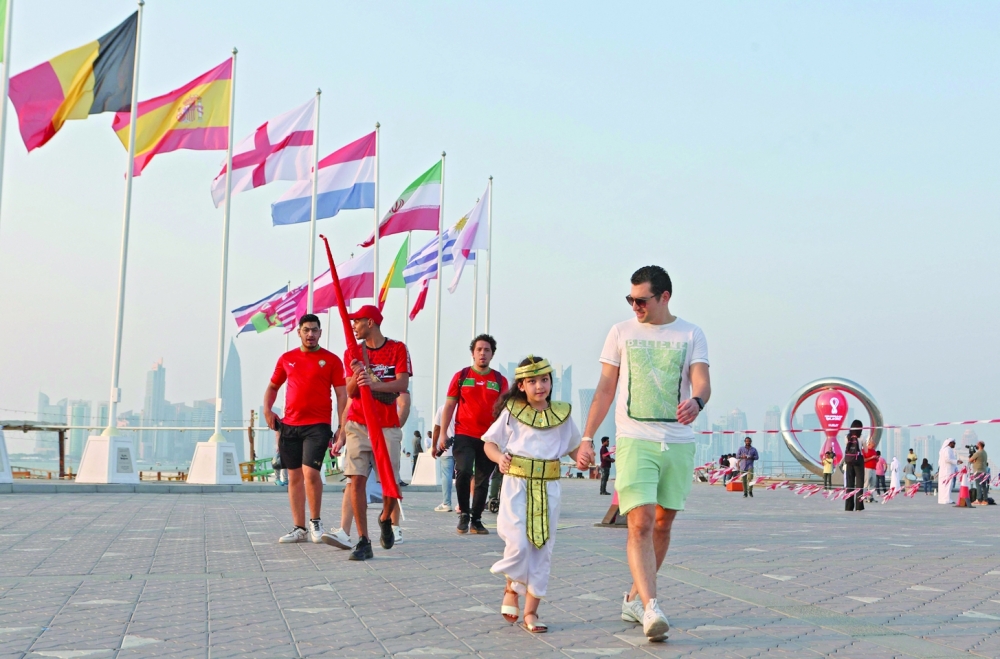 A picture taken on October 20, 2022, shows people walking past the Qatar 2022 Fifa World Cup countdown clock as it nears marking thirty days, in the Qatari capital Doha.  (Photo by Karim JAAFAR / AFP)