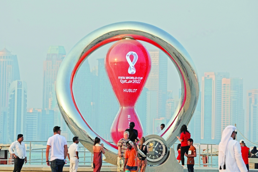 A picture taken on October 20, 2022, shows people walking past the Qatar 2022 FIFA World Cup countdown clock as it nears marking thirty days, in the Qatari capital Doha.  (Photo by Karim JAAFAR / AFP)

