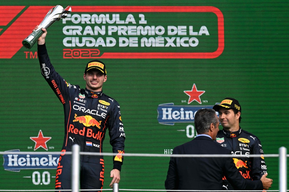TOPSHOT - Red Bull Racing's Dutch driver Max Verstappen celebrates on the podium next to second-place teammate Mexican driver Sergio Perez after winning the Formula One Mexico Grand Prix at the Hermanos Rodriguez racetrack in Mexico City on October 30, 2022.
  (Photo by Rodrigo ARANGUA / AFP)

