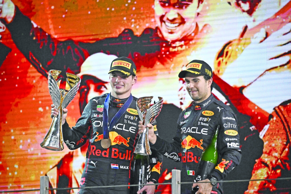 Red Bull's Dutch driver Max Verstappen (L) and Red Bull's Mexican driver Sergio Perez raise their trophies on the podium after the Abu Dhabi Formula One Grand Prix at the Yas Marina Circuit in the Emirati city of Abu Dhabi on November 20, 2022.  (Photo by Ben Stansall / AFP)

