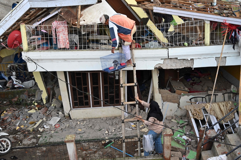 People save a cat from a damaged house following a 5.6-magnitude earthquake that killed at least 162 people, with hundreds injured and others missing in Cianjur on November 22, 2022.