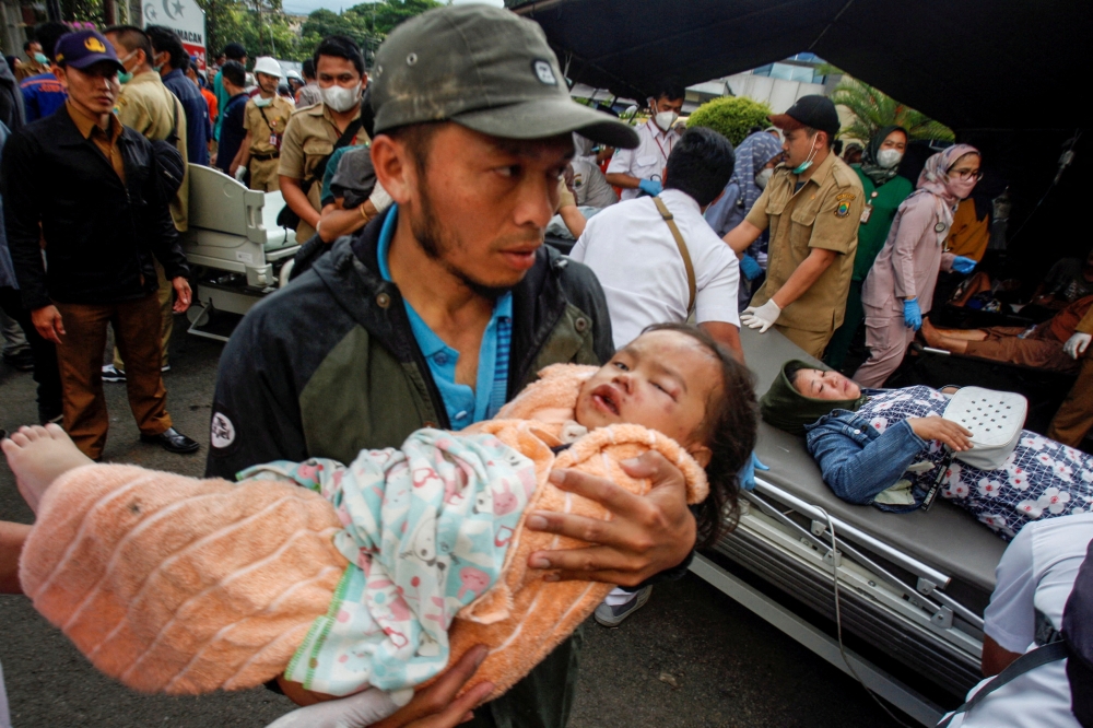 A man carries an injured child to receive treatment at a hospital, after an earthquake hit in Cianjur, West Java province, Indonesia