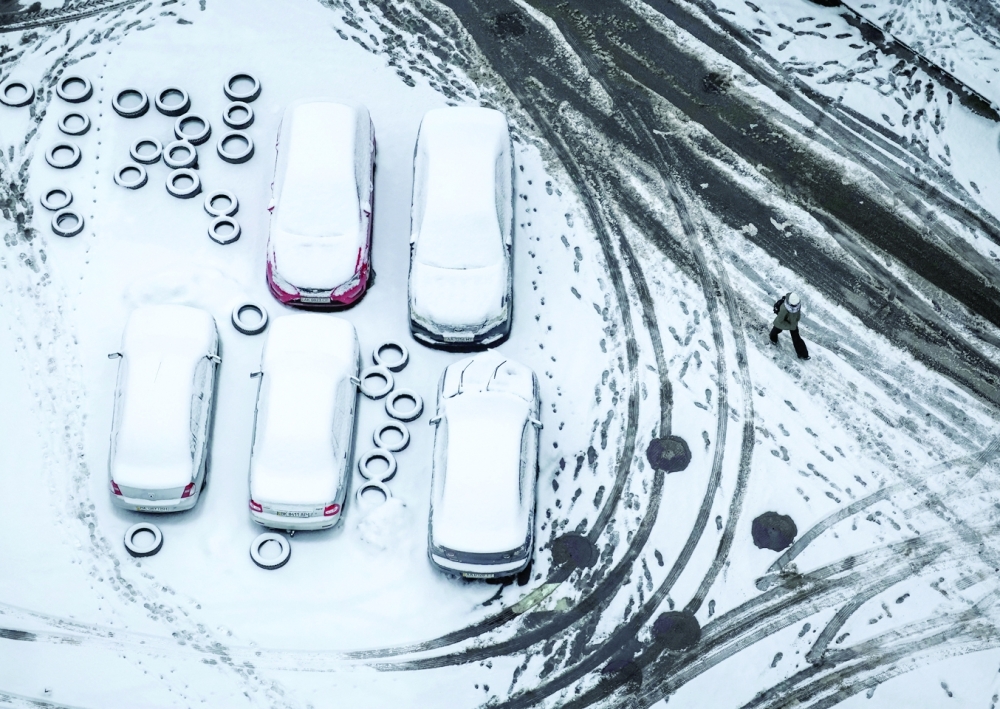 A pedestrian passes by cars covered in snow, in Kyiv, Ukraine, on Wednesday. - Reuters
