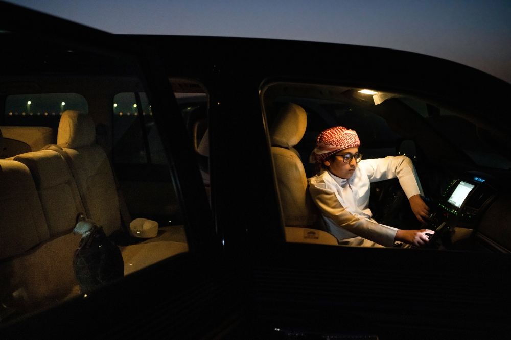 Talal al-Humaidi, 13, looks at his phone while his falcon sits in the back seat of the car after a training session outside Al Khor, Qatar, on Dec. 3, 2022. The best racing falcons are worth millions of dollars.   (Erin Schaff/The New York Times)