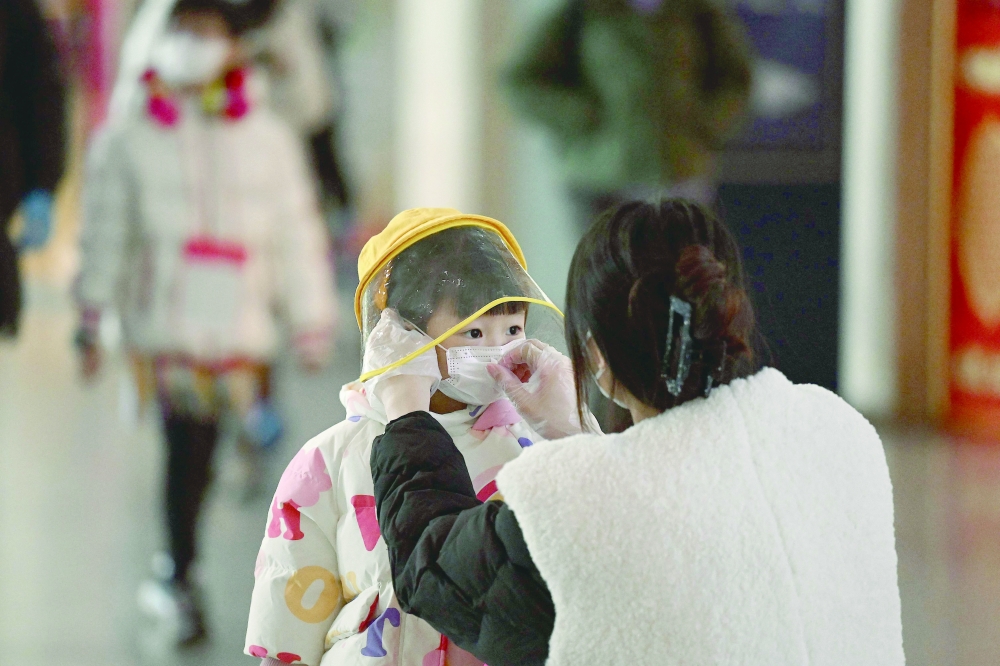 A woman arranges a face mask on a child's face in a departure terminal of the international airport in Beijing on Thursday. -- AFP
