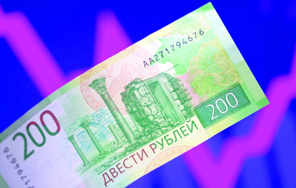 A Russian rouble banknote is seen in front of a descending and rising stock graph in this illustration. - Reuters
