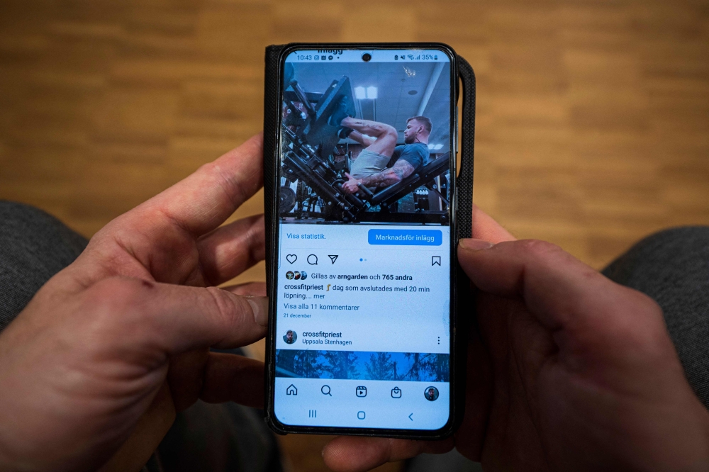 Oskar Arngarden scrolls through the videos posted on his Instagram account of him lifting weights and doing other exercises in Uppsala, Sweden. - AFP
