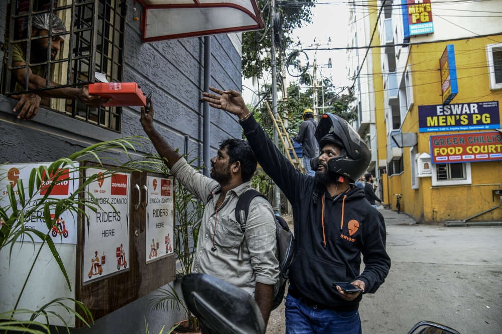 Shivam Neralwar, right, a delivery driver for Swiggy, picks up a food order in Hyderabad, India, Dec. 2, 2022 (Atul Loke/The New York Times)