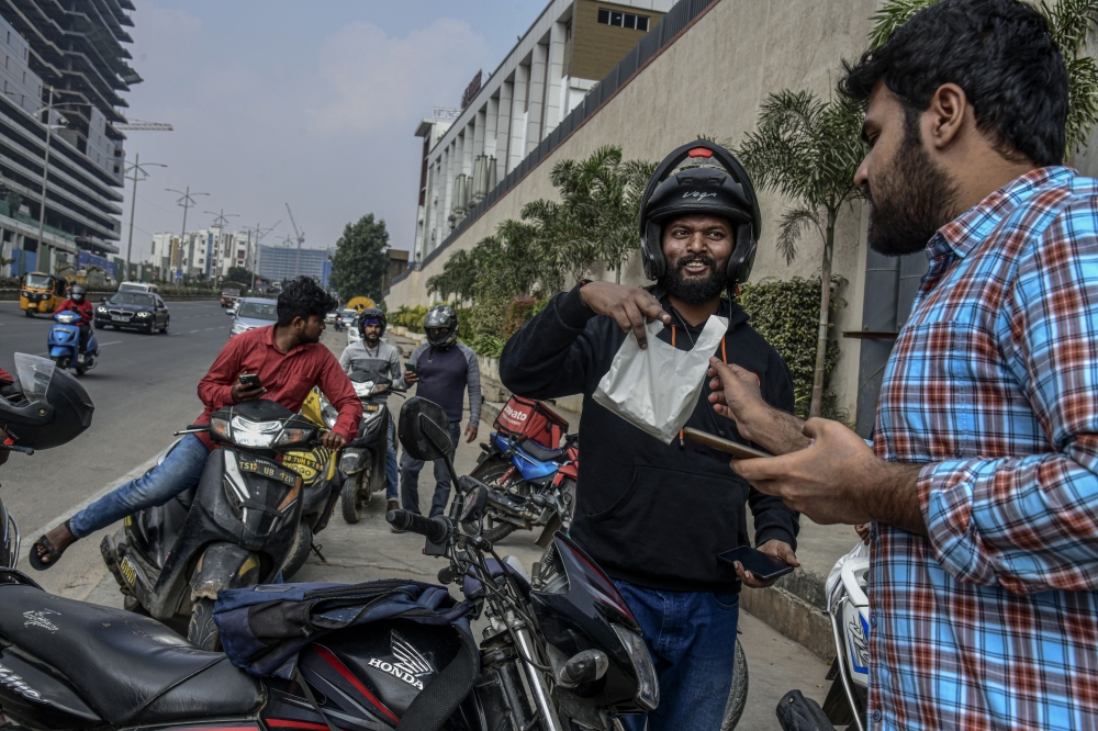 Shivam Neralwar, center, a delivery driver for Swiggy, delivers an order to a customer at an office in Hyderabad, India, Dec. 2, 2022. (Atul Loke/The New York Times)