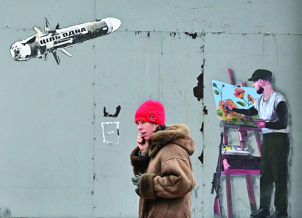A man speaks on a mobile phone as he walks past a mural depicting a flying missile and an artist at his easel, in the centre of the Ukrainian capital of Kyiv on Monday.-- AFP