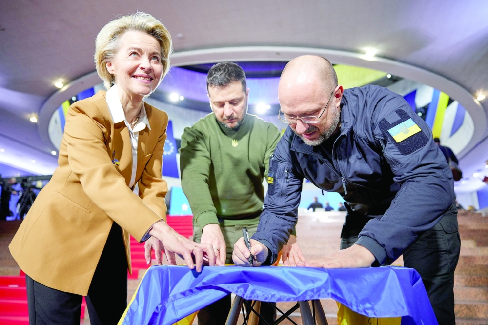 Ukraine's President Volodymyr Zelenskiy, Prime Minister Denys Shmyhal and European Commission President Ursula von der Leyen sign a Ukrainian national flag before start of EU summit in Kyiv. -- Reuters