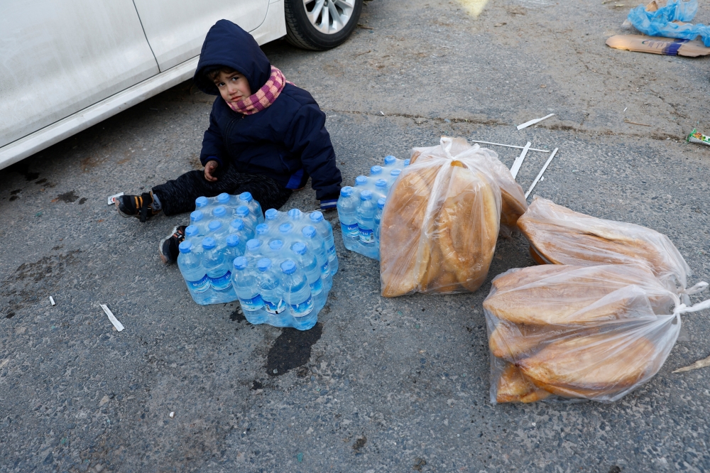 A child is seated next to food and water supplies following an earthquake in Kahramanmaras, Turkey, February 8, 2023. REUTERS/Suhaib Salem