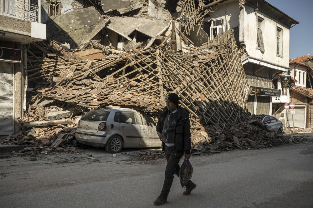 An earthquake survivor passes a collapsed building in Antakya, in Hatay Province, Turkey, on Thursday, Feb. 9, 2023. (Sergey Ponomarev/The New York Times)