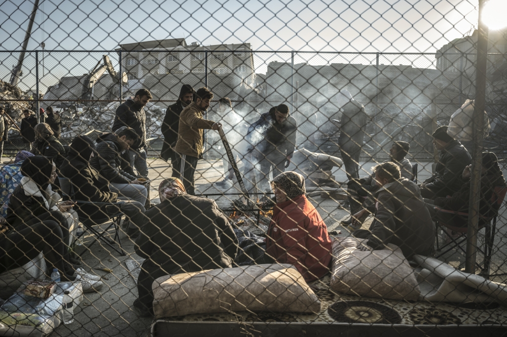 Earthquake survivors gather around a bonfire near collapsed buildings in Antakya, in Hatay Province, Turkey, on Feb. 8, 2023. (Sergey Ponomarev/The New York Times)