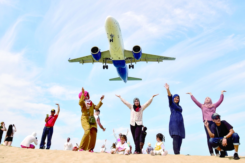 Tourists pose for picture on Mai Khao Beach as a plane lands at Phuket International Airport in Phuket province, Thailand, on Tuesday. -- AFP