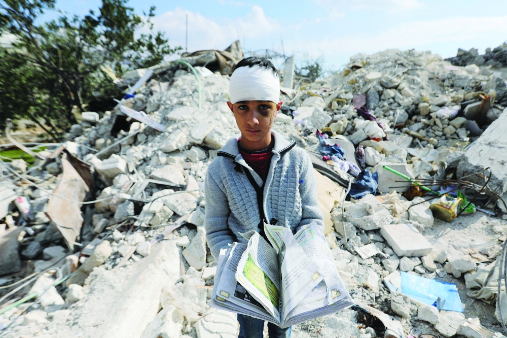 A Syrian boy, who lost his family and was also wounded as a result of the deadly earthquake, carries a book as he stands amid the rubble of his family home in the town of Jindayris, in Aleppo province. - AFP