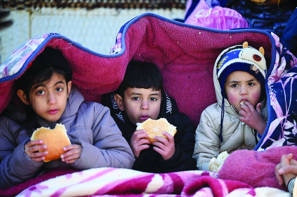 Children eat bread as they sit under a cover  in the southeastern Turkish city of Kahramanmaras, two days after a strong earthquake struck the region. - AFP