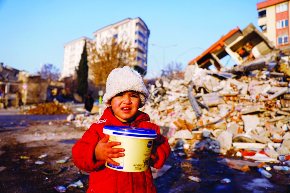 A child holding a plastic container looks on amid rubble in the aftermath of a deadly earthquake in Kahramanmaras. - Turkey