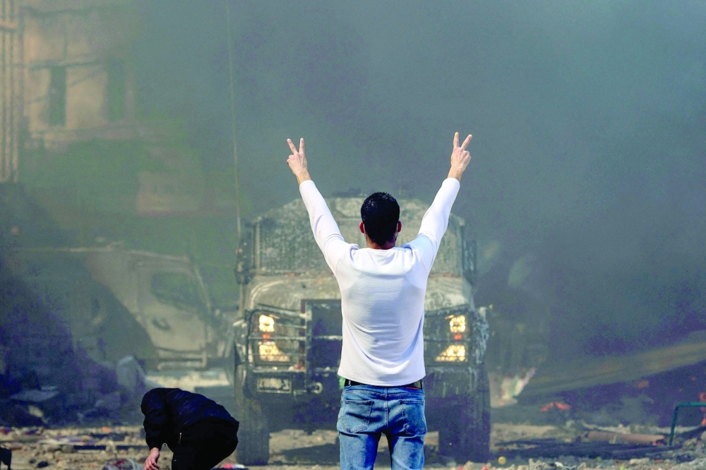 A Palestinian man flashes the victory sign as he faces an Israeli military vehicle, during a raid on Nablus on Wednesday. — AFP