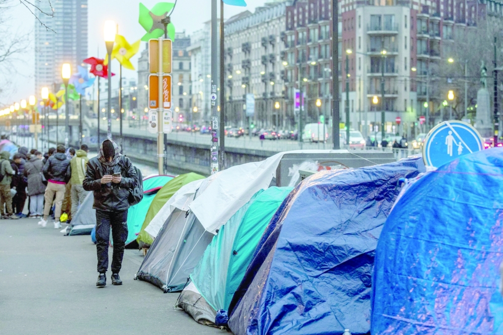A man is seen walking near the tents in Brussels, where a long line has formed along the canal as new tents are set up every day. Many asylum seekers still lack proper housing, despite having their demands approved. Authorities are actively searching for more emergency hotel rooms to accommodate them. -- AFP