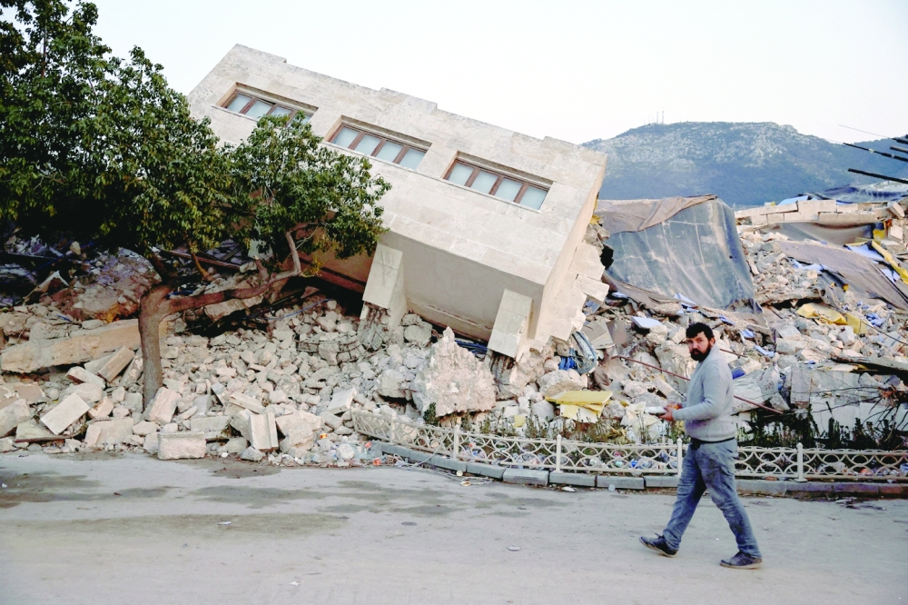 A man walks by a collapsed building and rubble in the aftermath of a deadly earthquake, in Antakya, Hatay province. - Reuters File 

