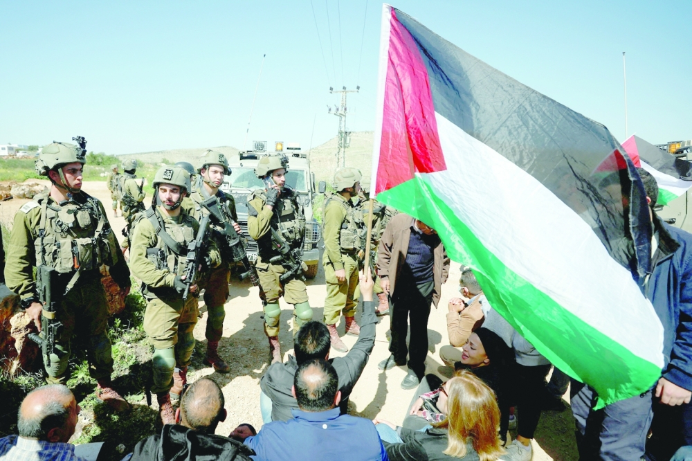 Palestinians raise their flag as they face off with Israeli forces during a protest against a new Israeli settlement near Ramallah in the Israeli-occupied West Bank. - Reuters
