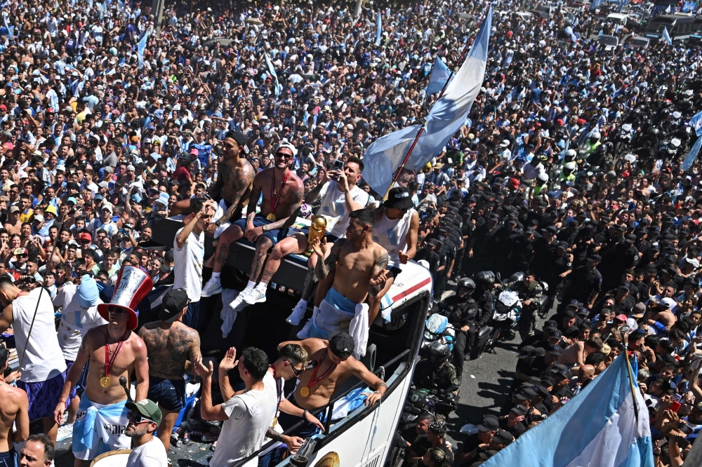 (FILES) In this file photo taken on December 20, 2022, Argentina's players celebrate on board a bus with a sign reading "World Champions" with supporters after winning the Qatar 2022 World Cup tournament as they tour through Buenos Aires' downtown.  More than 1.5 million Argentina fans applied for 63,000 tickets for the team's first appearance, in a friendly against Panama, since lifting the football World Cup in Qatar. 
Tickets for the match in Buenos Aires on March 23, 2023, sold out in two hours, according to the Deportick website, as local media said the virtual ticket line drew 1.5 million people.
 (Photo by Luis ROBAYO / AFP)

