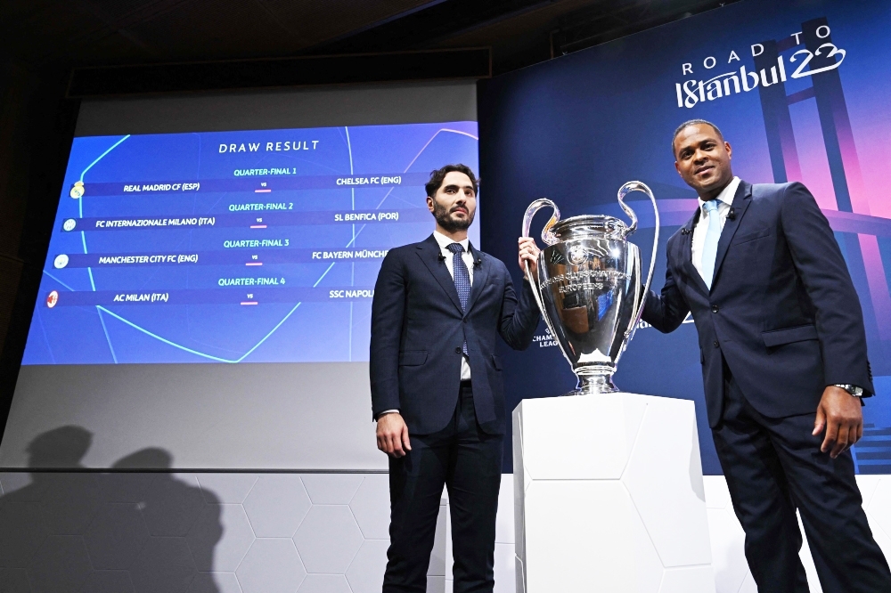 UEFA Champions League final ambassadors Turkish former footballer Hamit Altintop (L) and Dutch former footballer Patrick Kluivert pose next to the draw result for the quarterfinal and the trophy of the 2022-2023 Uefa Champions League tournament, in Nyon. -- AFP