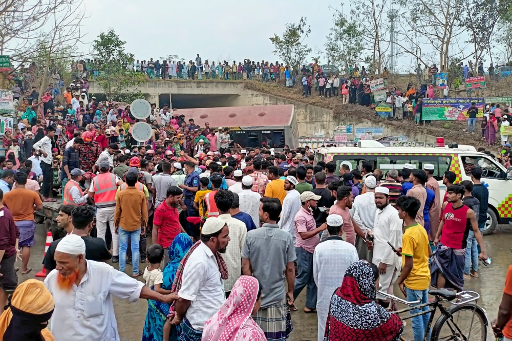 People gather after a bus met with an accident in Madaripur on March 19, 2023. At least 17 people were killed and up to 25 were injured Sunday in Bangladesh after a bus smashed through a highway fence and plunged into a roadside ditch, according to police. (Photo by AFP)


