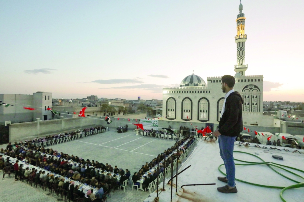 A man looks on from a rooftop as people gather for a collective Iftar fast-breaking meal in a school courtyard in the village of Bizzah in Aleppo province during Ramadhan. - AFP