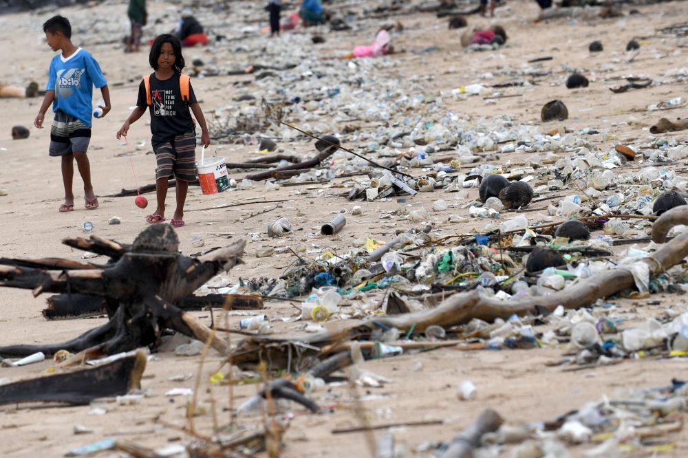 Children walk past plastic and other debris washed ashore at Kedonganan Beach, Badung Regency, on Indonesia's resort island of Bali on April 12, 2023.